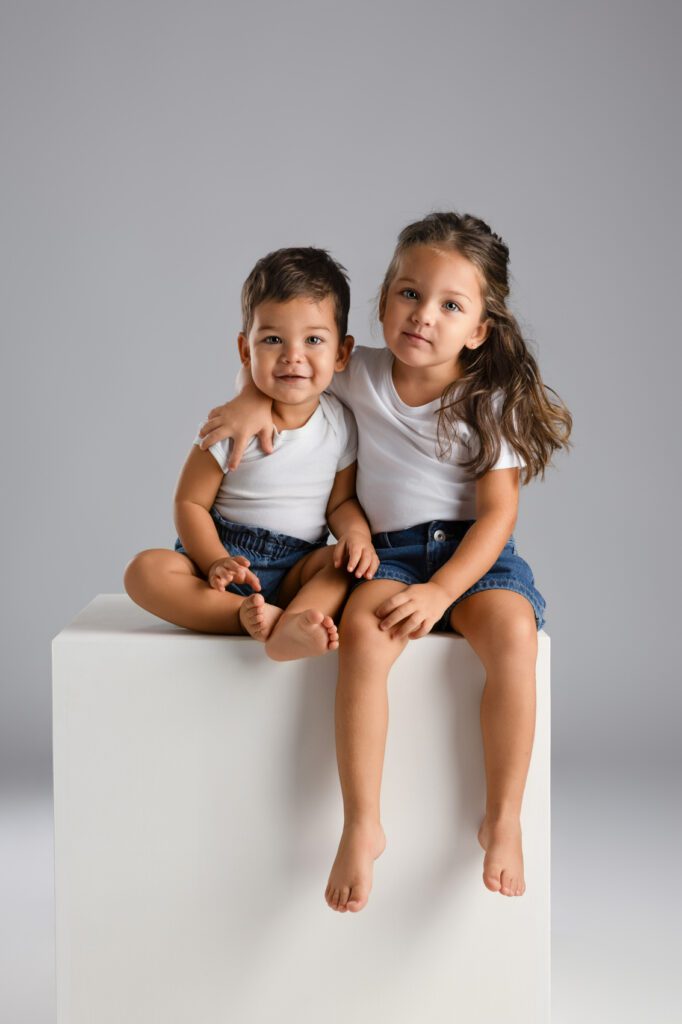Deux enfants complices en blanc et jeans : cohérence vestimentaire pour une séance en studio.